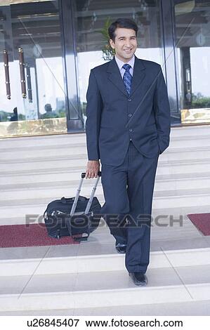 Stock Photo - Portrait of a businessman pulling his luggage and smiling. Fotosearch