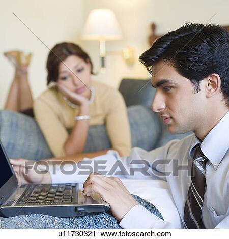 Side profile of a businessman working on a laptop with a young woman lying on the bed in the background View Large Photo Image Stock Image - Side profile of a businessman working on a laptop with a young woman lying on the bed in the background. Fotosearch