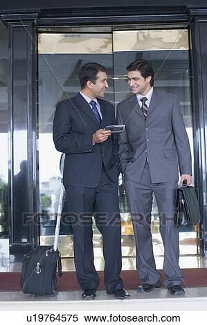 Stock Photography - Two businessmen standing in front of a door and smiling. Fotosearch