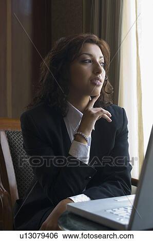 Stock Photograph - Businesswoman sitting in front of a laptop and thinking. Fotosearch