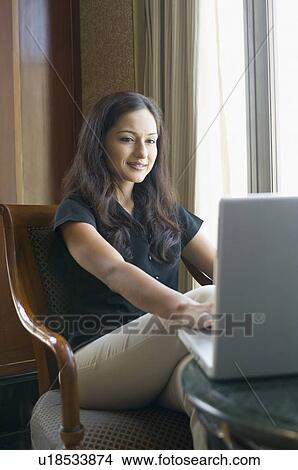 Picture - Businesswoman sitting on a chair and using a laptop. Fotosearch