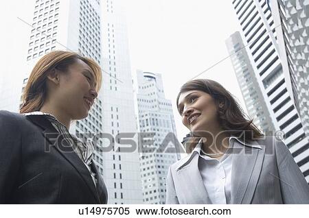 Low angle view of two businesswomen standing together and smiling, Singapore View Large Photo Image Stock Photography - Low angle view of two businesswomen standing together and smiling, Singapore. Fotosearch