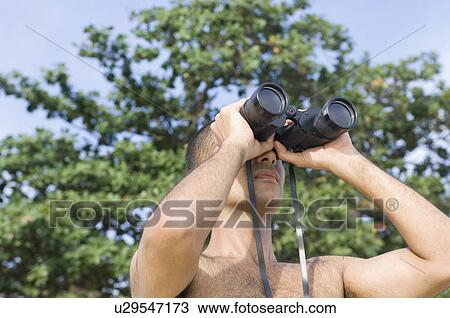 Stock Image - Close-up of a young man looking through binoculars. Fotosearch