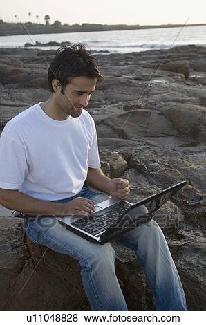 High angle view of a young man working on a laptop at a coast, Madh Island, Mumbai, Maharashtra, India View Large Photo Image Stock Photo - High angle view of a young man working on a laptop at a coast, Madh Island, Mumbai, Maharashtra, India. Fotosearch