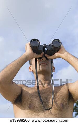 Low angle view of a young man looking through a pair of binoculars View Large Photo Image Stock Photograph - Low angle view of a young man looking through a pair of binoculars. Fotosearch