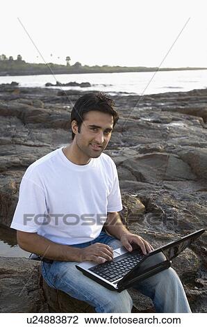Portrait of a young man holding a laptop on his lap and smiling, Madh Island, Mumbai, Maharashtra, India View Large Photo Image Stock Image - Portrait of a young man holding a laptop on his lap and smiling, Madh Island, Mumbai, Maharashtra, India. Fotosearch