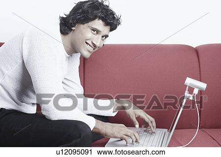 Portrait of a young man sitting on a couch in front of a laptop View Large Photo Image Stock Image - Portrait of a young man sitting on a couch in front of a laptop. Fotosearch