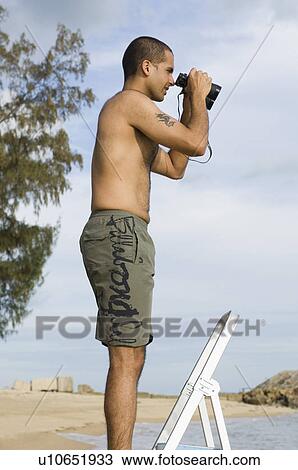 Side profile of a young man looking through binoculars on the beach View Large Photo Image Stock Image - Side profile of a young man looking through binoculars on the beach. Fotosearch