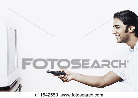 Stock Image - Side profile of a young man operating a remote control. Fotosearch