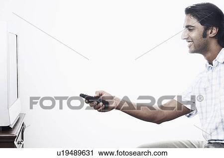 Stock Image - Side profile of a young man operating a remote control. Fotosearch