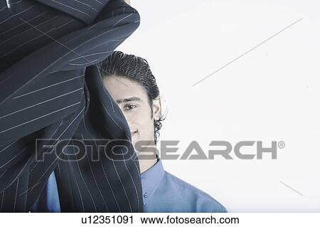 Young man holding a coat in front of his face View Large Photo Image Stock Image - Young man holding a coat in front of his face. Fotosearch