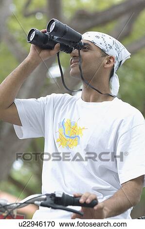 Stock Image - Young man looking through binoculars and smiling. Fotosearch