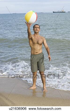 Stock Photograph - Young man playing on the beach with a beach ball. Fotosearch