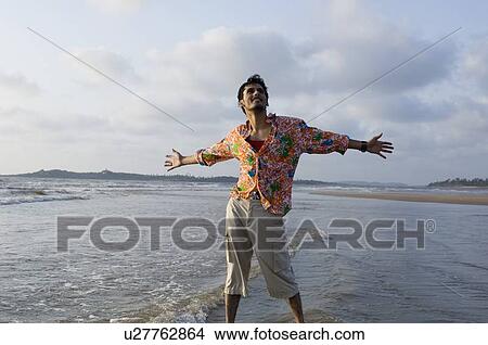 Young man standing on the beach with his arm outstretched View Large Photo Image Picture - Young man standing on the beach with his arm outstretched. Fotosearch
