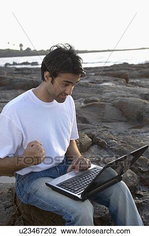 Young man working on a laptop on a coast, Madh Island, Mumbai, Maharashtra, India View Large Photo Image Stock Image - Young man working on a laptop on a coast, Madh Island, Mumbai, Maharashtra, India. Fotosearch