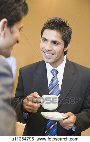 Stock Photography - Close-up of a businessman holding a cup of tea and talking with his colleague. Fotosearch
