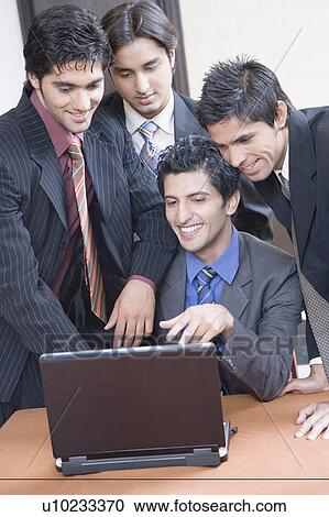 Four businessmen using a laptop and smiling View Large Photo Image Stock Image - Four businessmen using a laptop and smiling. Fotosearch
