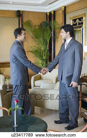 Side profile of two businessmen shaking hands and smiling in a lobby View Large Photo Image Stock Photo - Side profile of two businessmen shaking hands and smiling in a lobby. Fotosearch