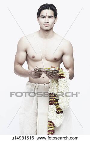 Stock Photograph - Portrait of a young man in traditional clothing holding a garland. Fotosearch
