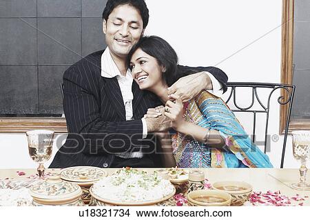 Picture - Young couple with arm around sitting at the dining table. Fotosearch