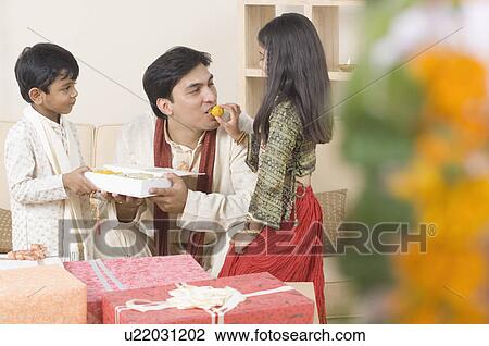 Stock Image - Girl feeding her father with diwali sweets. Fotosearch