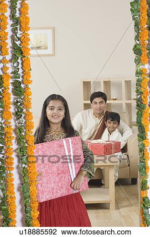 Girl holding a diwali gift with her father and brother sitting in the background View Large Photo Image Stock Image - Girl holding a diwali gift with her father and brother sitting in the background. Fotosearch