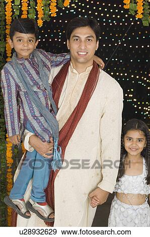 Portrait of a young man carrying his son with his daughter standing beside him View Large Photo Image Stock Photo - Portrait of a young man carrying his son with his daughter standing beside him. Fotosearch