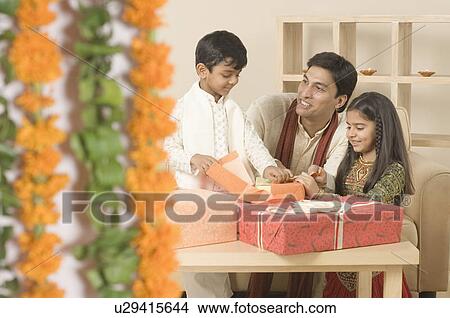 Picture - Young man sitting with his children and opening diwali gifts. Fotosearch