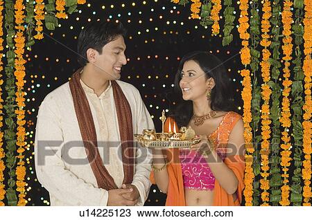 Young woman holding a diwali thali with a young man standing beside her View Large Photo Image Stock Image - Young woman holding a diwali thali with a young man standing beside her. Fotosearch