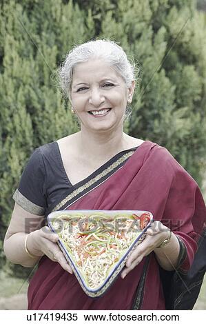 Portrait of a mature woman holding a dish of sliced vegetables View Large Photo Image Stock Photography - Portrait of a mature woman holding a dish of sliced vegetables. Fotosearch