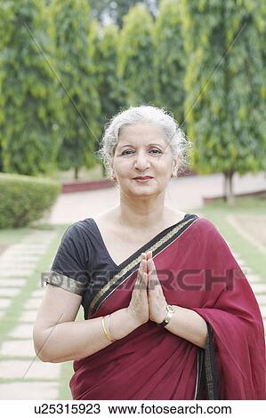 Stock Image - Portrait of a mature woman standing with her hands together. Fotosearch