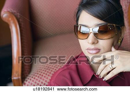 Stock Image - Close-up of a young woman wearing sunglasses with her hand on her chin. Fotosearch