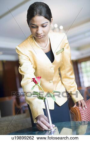 Stock Image - Low angle view of a waitress putting flower vase on a table in a lobby. Fotosearch