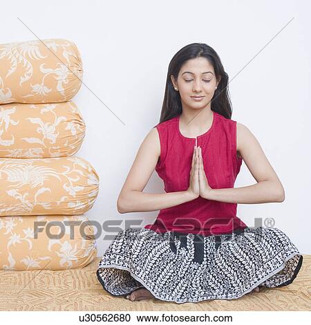 Stock Image - Young woman sitting on the bed in a prayer position. Fotosearch