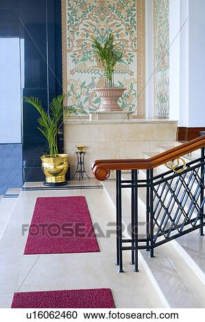 Stock Image - Doormats and potted plants in front of a staircase. Fotosearch