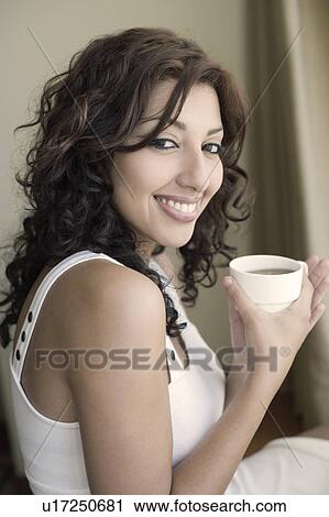 Stock Image - Portrait of a young woman holding a cup of tea and smiling. Fotosearch