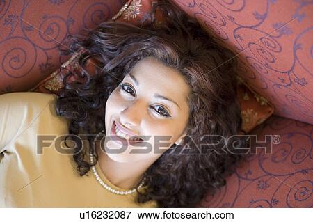 Stock Photo - Portrait of a young woman lying on a couch and smiling. Fotosearch