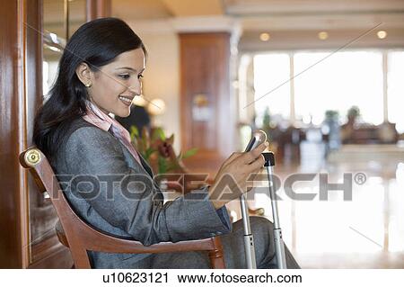 Stock Image - Side profile of a businesswoman text messaging on a mobile phone and smiling. Fotosearch