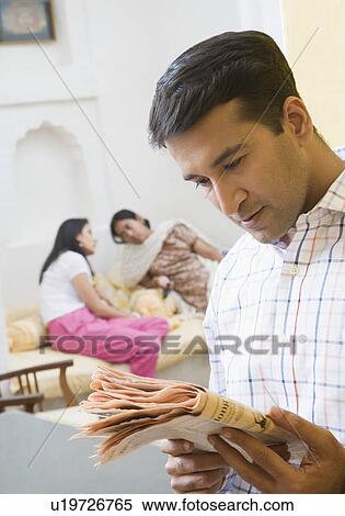 Stock Photography - Close-up of a mid adult man reading a newspaper with two mid adult women sitting behind him. Fotosearch