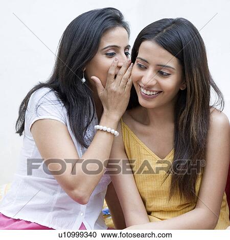 Mid adult woman whispering into her friend's ear View Large Photo Image Stock Image - Mid adult woman whispering into her friend's ear. Fotosearch