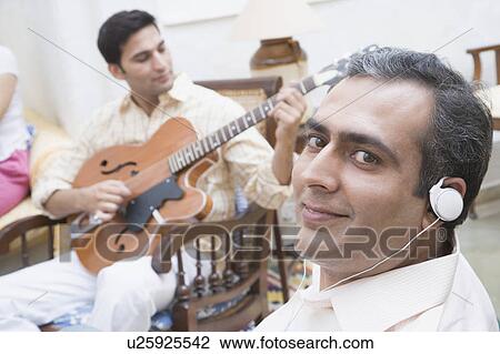 Portrait of a mid adult man wearing headphones and a young man playing guitar in front of him View Large Photo Image Stock Image - Portrait of a mid adult man wearing headphones and a young man playing guitar in front of him. Fotosearch
