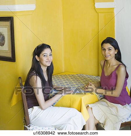 Portrait of two young women sitting at a table and smiling View Large Photo Image Stock Image - Portrait of two young women sitting at a table and smiling. Fotosearch