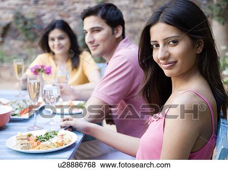 Young couple sitting with a mid adult woman at a dining table View Large Photo Image Stock Photo - Young couple sitting with a mid adult woman at a dining table. Fotosearch