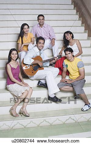 Young man playing a guitar with his friends sitting around him View Large Photo Image Picture - Young man playing a guitar with his friends sitting around him. Fotosearch