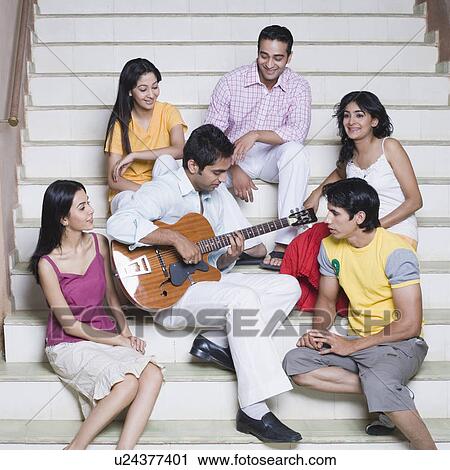 Young man playing a guitar with his friends sitting beside him View Large Photo Image Stock Image - Young man playing a guitar with his friends sitting beside him. Fotosearch