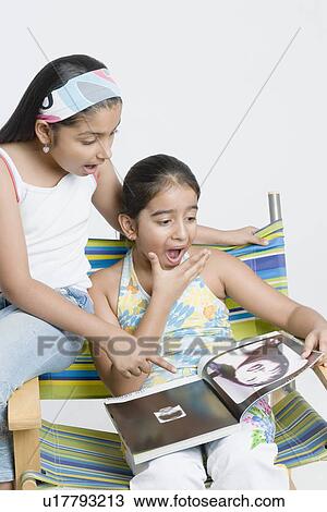 Stock Image - Close-up of a girl sitting with her sister and watching a magazine. Fotosearch