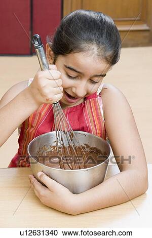 Stock Image - Close-up of a girl stirring chocolate sauce with an egg beater. Fotosearch