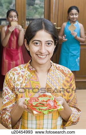 Close-up of a mid adult woman holding a sandwich with her daughters in the background View Large Photo Image Stock Image - Close-up of a mid adult woman holding a sandwich with her daughters in the background. Fotosearch