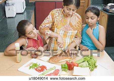 Picture - Close-up of a mid adult woman making sandwiches with her daughters. Fotosearch