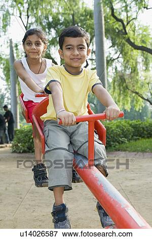 Girl and a boy sitting on a seesaw View Large Photo Image Stock Photo - Girl and a boy sitting on a seesaw. Fotosearch